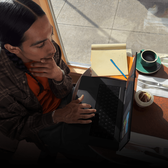Uma pessoa em um café trabalhando em um MacBook Pro que não está conectado na tomada