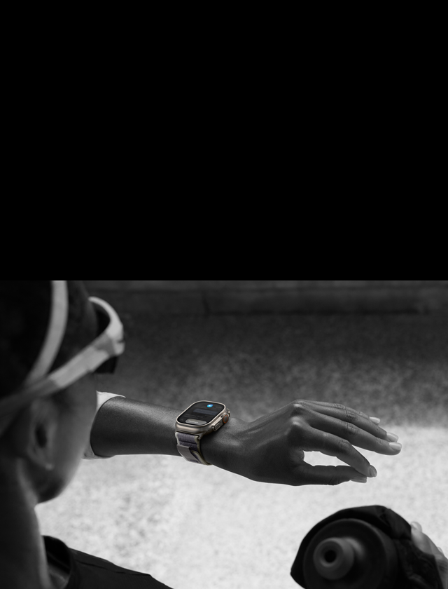 Imagem de uma corredora olhando para o Apple Watch Ultra 2 no pulso esquerdo dela enquanto faz o gesto com dois toques com os dedos indicador e polegar da mão esquerda.